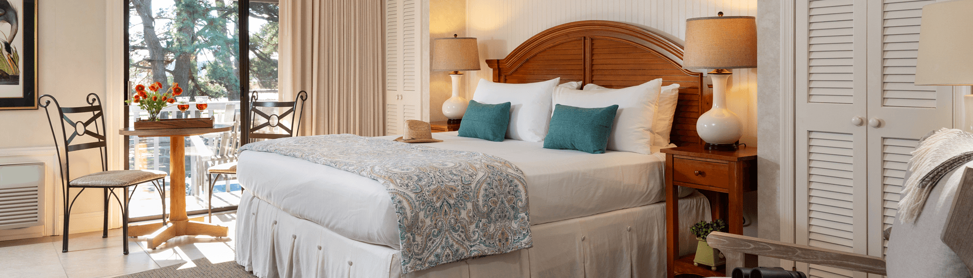 Cozy hotel room featuring a bed with decorative pillows, a wooden table with flowers, and a small seating area.