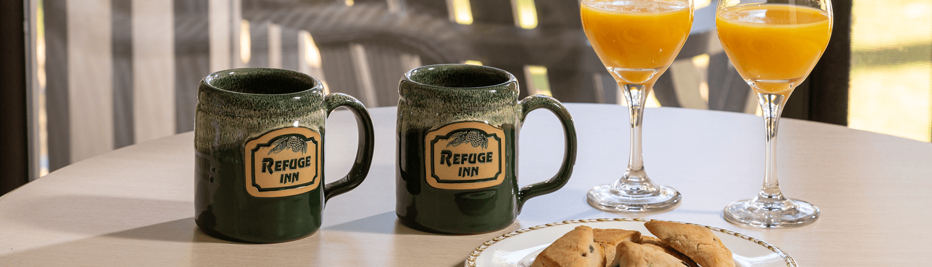 Two green mugs and two glasses of orange juice sit on a table next to a plate of pastries.