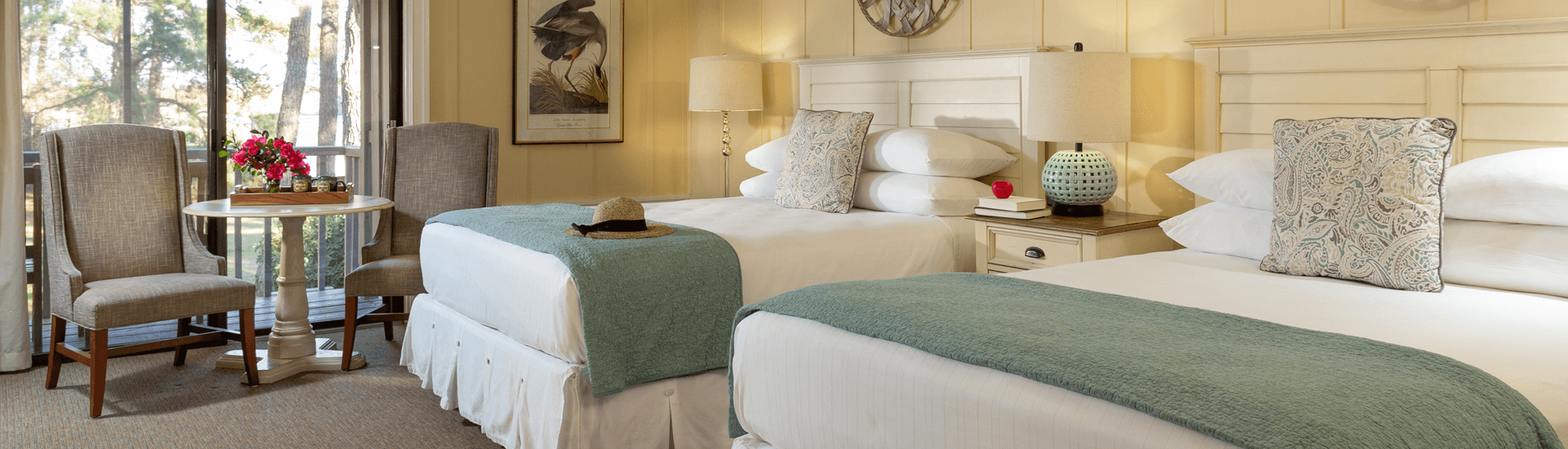 A cozy hotel room featuring two beds, comfortable chairs, and a small table with flowers.