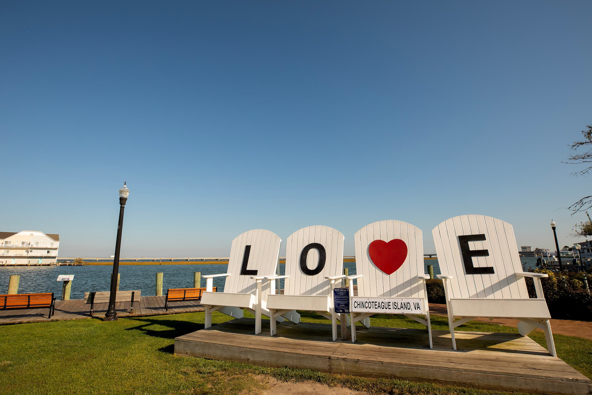 Oversized white Adirondack chairs spelling "LOVE" with a heart on Chincoteague Island, VA, by the water.