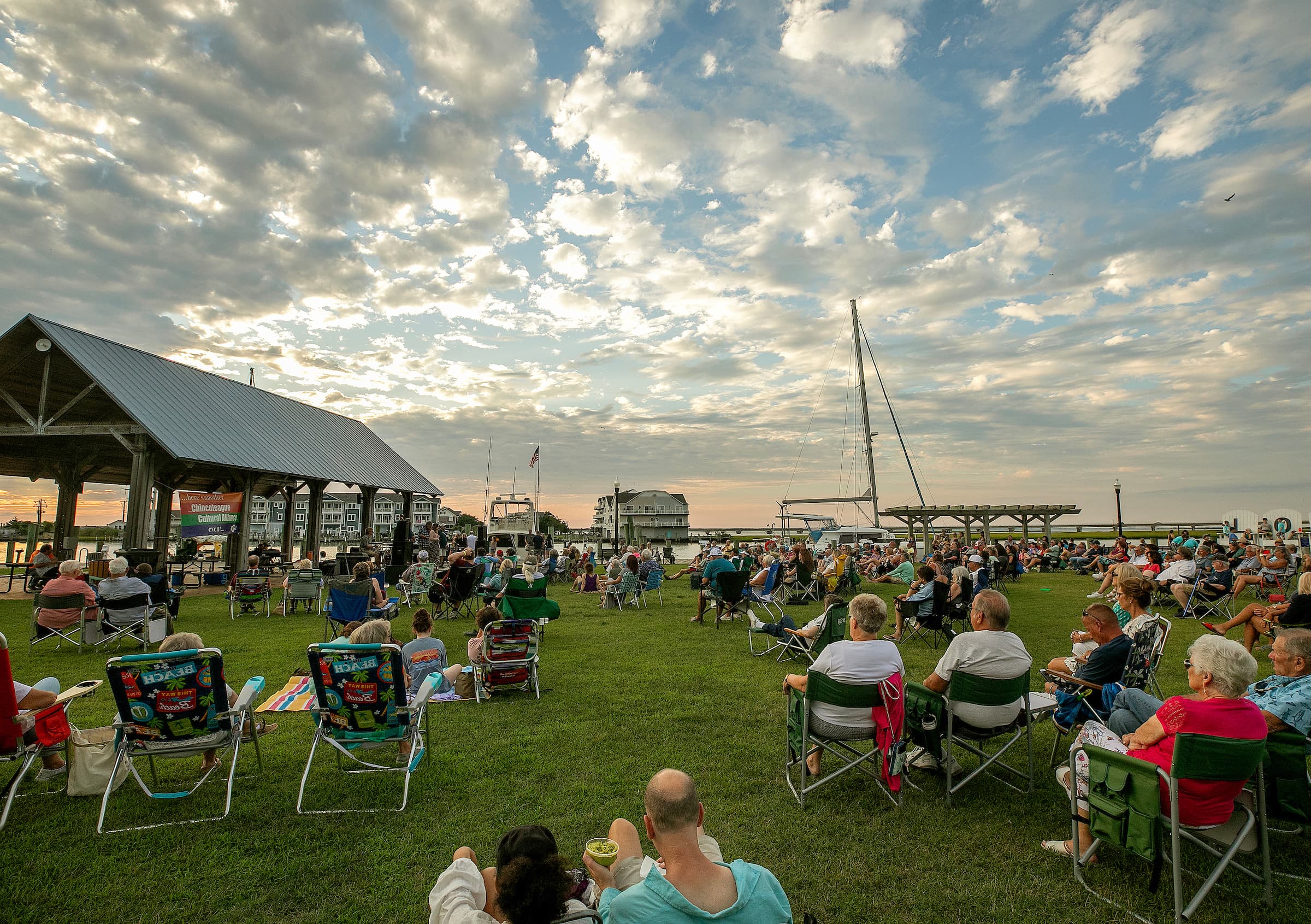 A large crowd gathers on the grass for an outdoor event under a cloudy sky.