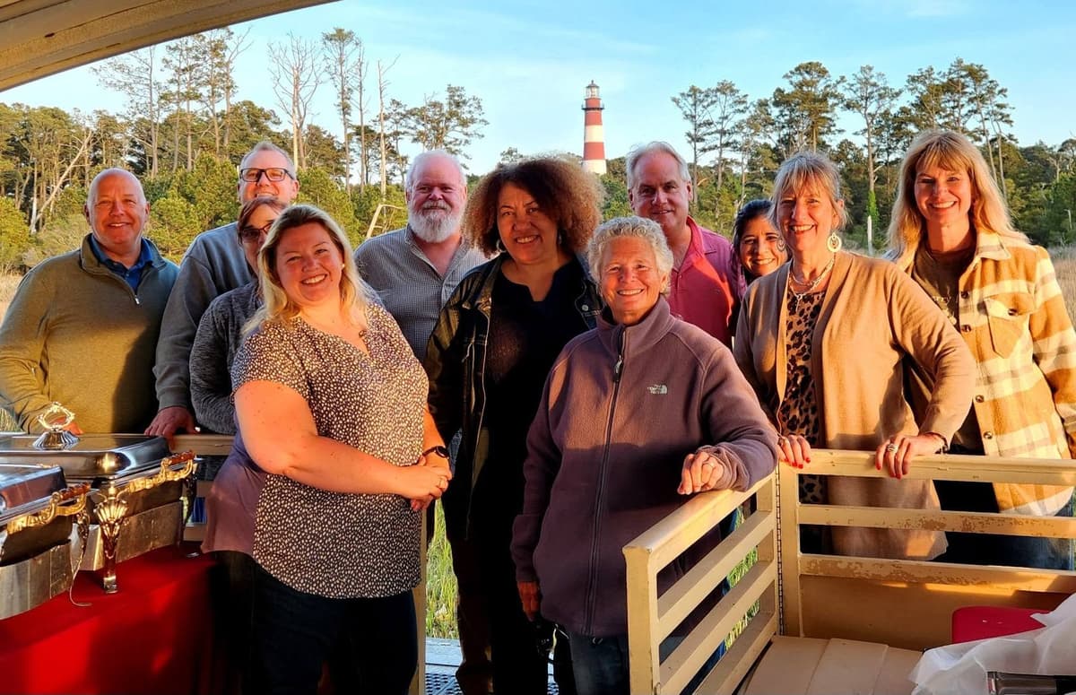 A group of twelve on a boat tour off Chincoteague Island, the Assateague Lighthouse behind them.