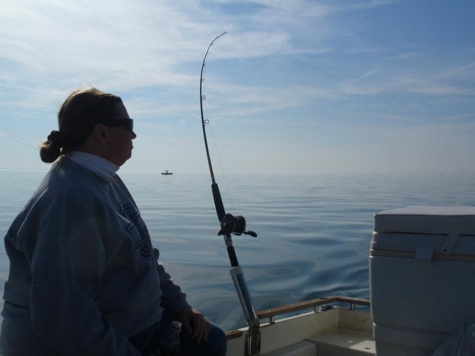 A person sits on a boat, gazing out at calm waters while holding a fishing rod.