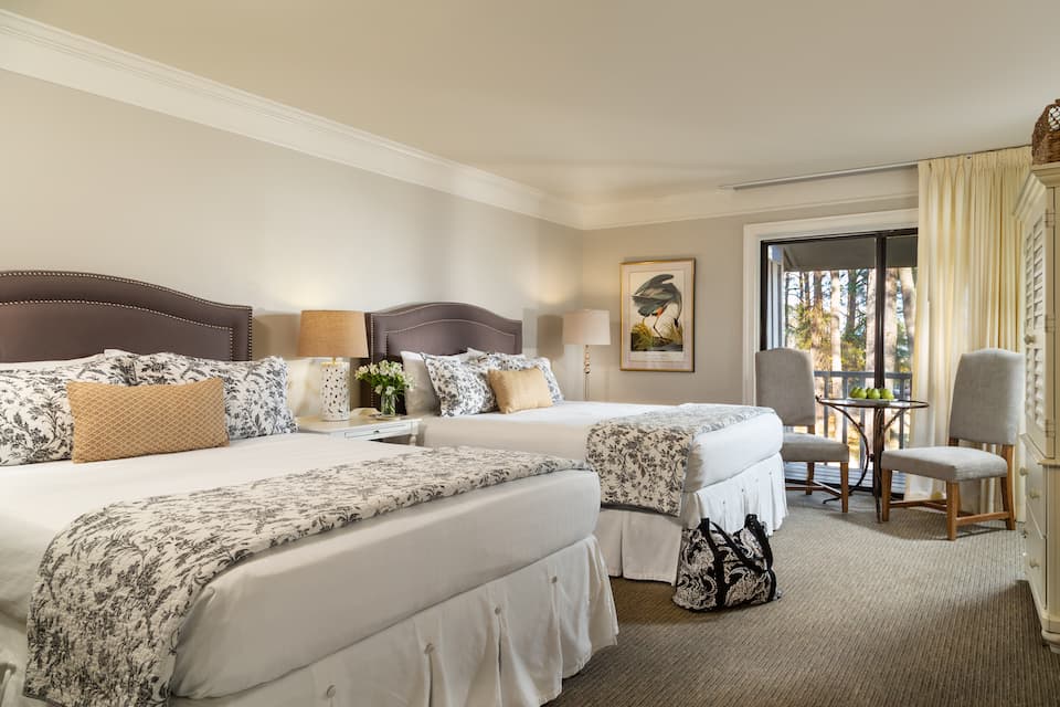 A cozy hotel room featuring two beds, a small dining area, and a balcony.