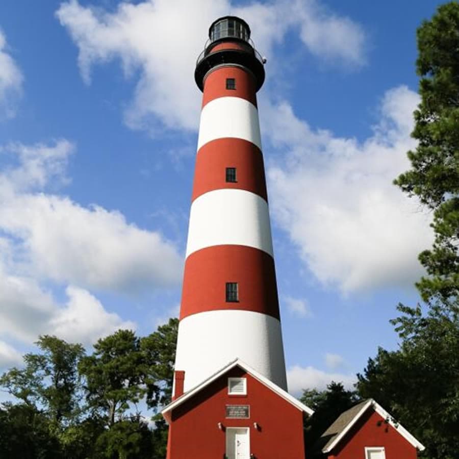 A tall, striped lighthouse stands against a blue sky with scattered clouds.