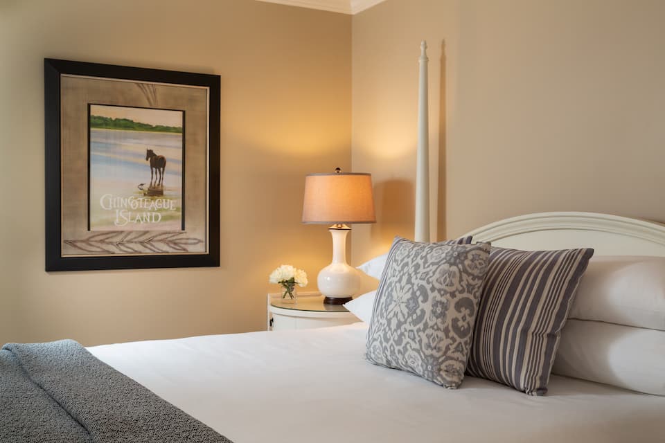 A cozy bedroom featuring a bed, decorative pillows, a bedside lamp, and wall art.