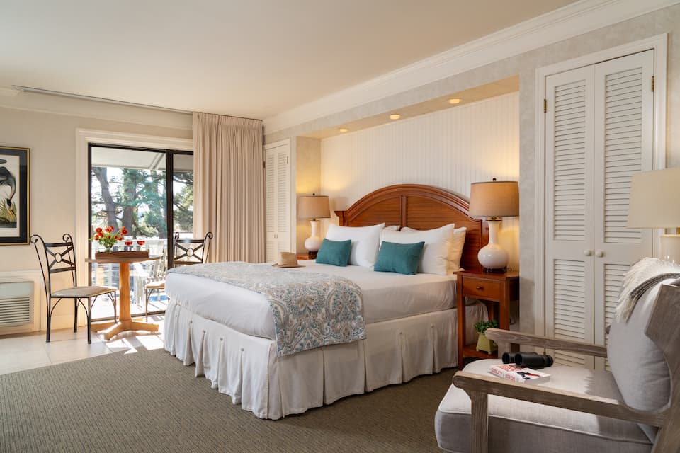 A cozy hotel room featuring a queen bed, two bedside lamps, and a small dining table by a window.