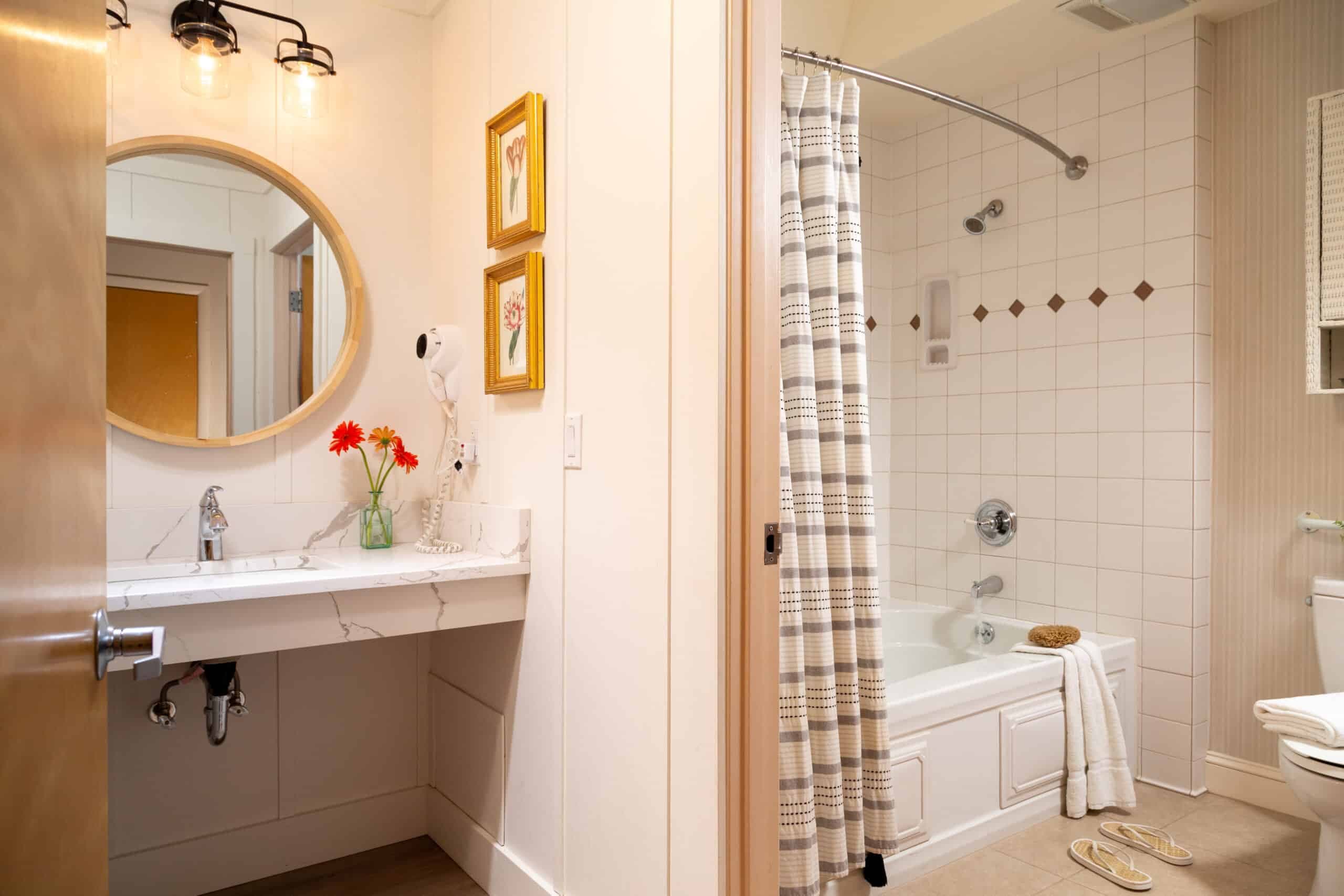 A stylish bathroom featuring a round mirror, a sink with flowers, and a tub with a shower curtain.