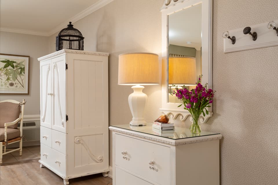 A stylish entryway featuring a white cabinet, a lamp, a mirror, and a vase of flowers.
