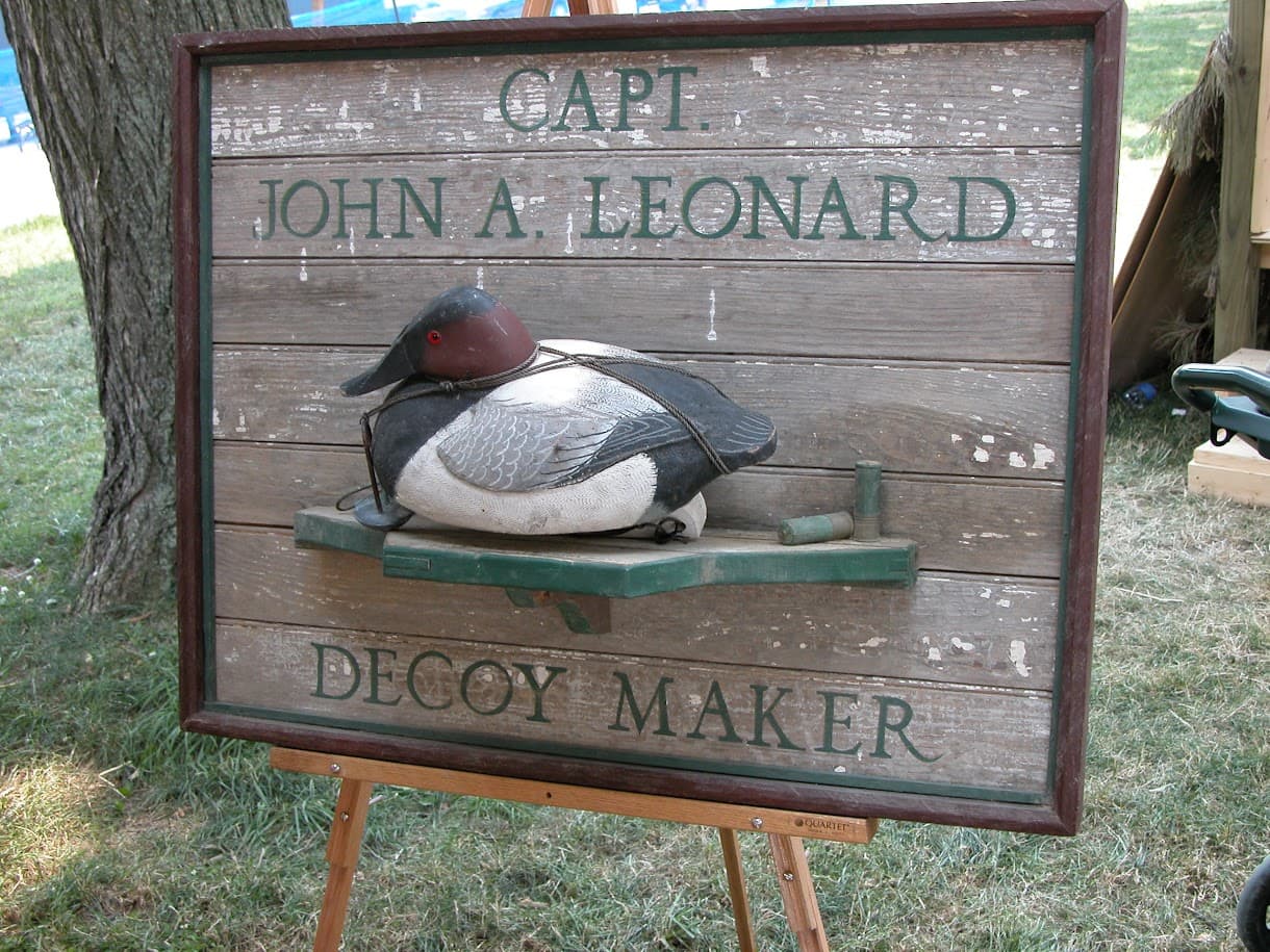 A wooden sign featuring a painted duck decoy and the text "Capt. John A. Leonard Decoy Maker."