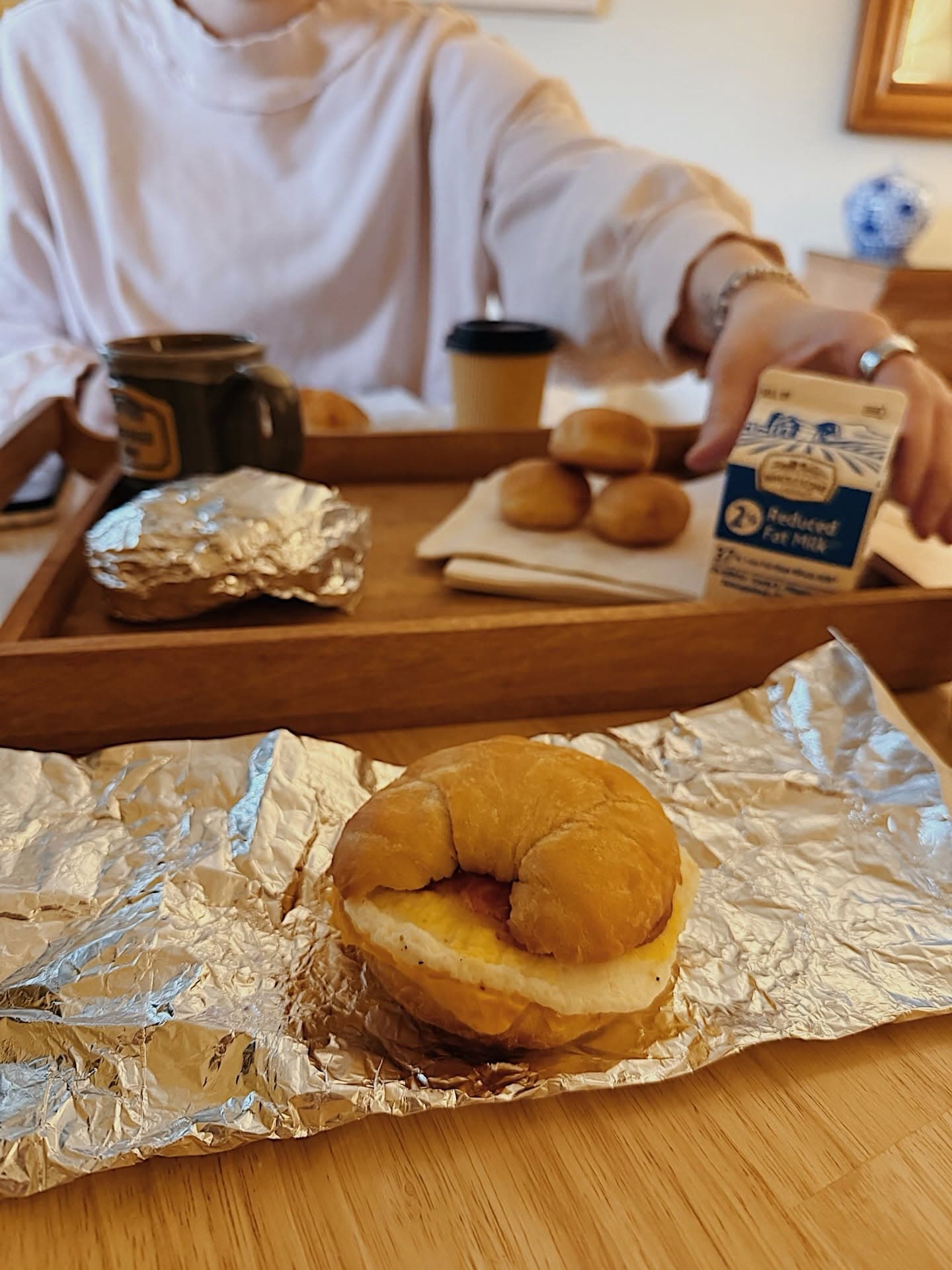 A breakfast tray with a croissant sandwich, mini pastries, a coffee cup, and a carton of milk.