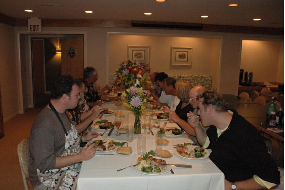 A group of people is enjoying a meal at a long table decorated with flowers.
