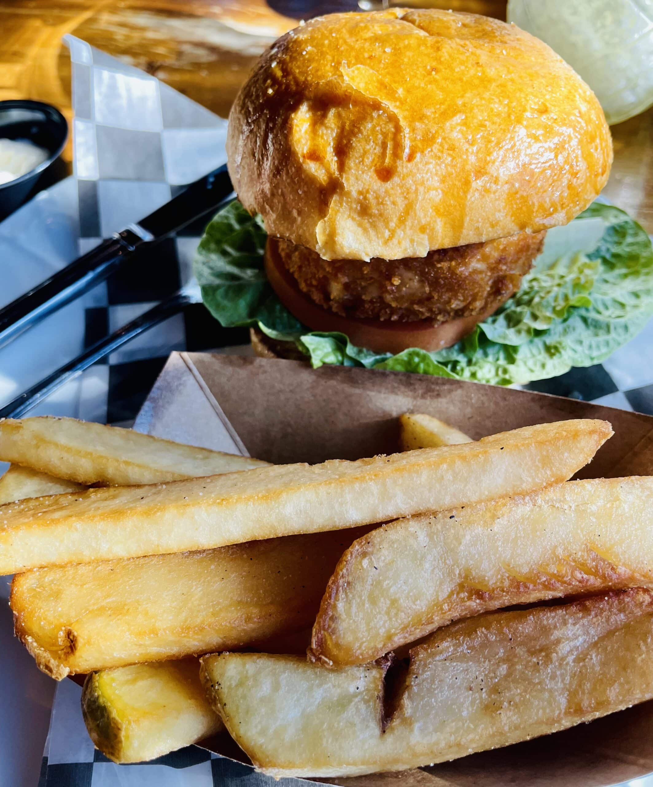 A golden fried chicken sandwich sits on lettuce beside a serving of crispy French fries.
