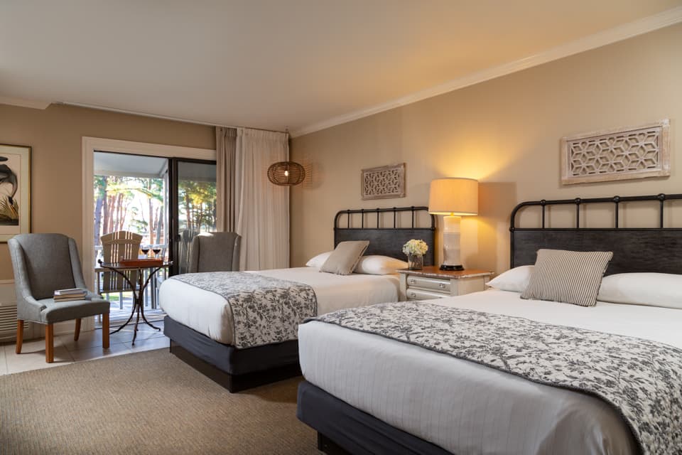 A cozy hotel room featuring two queen beds, a seating area, and a view of a patio.