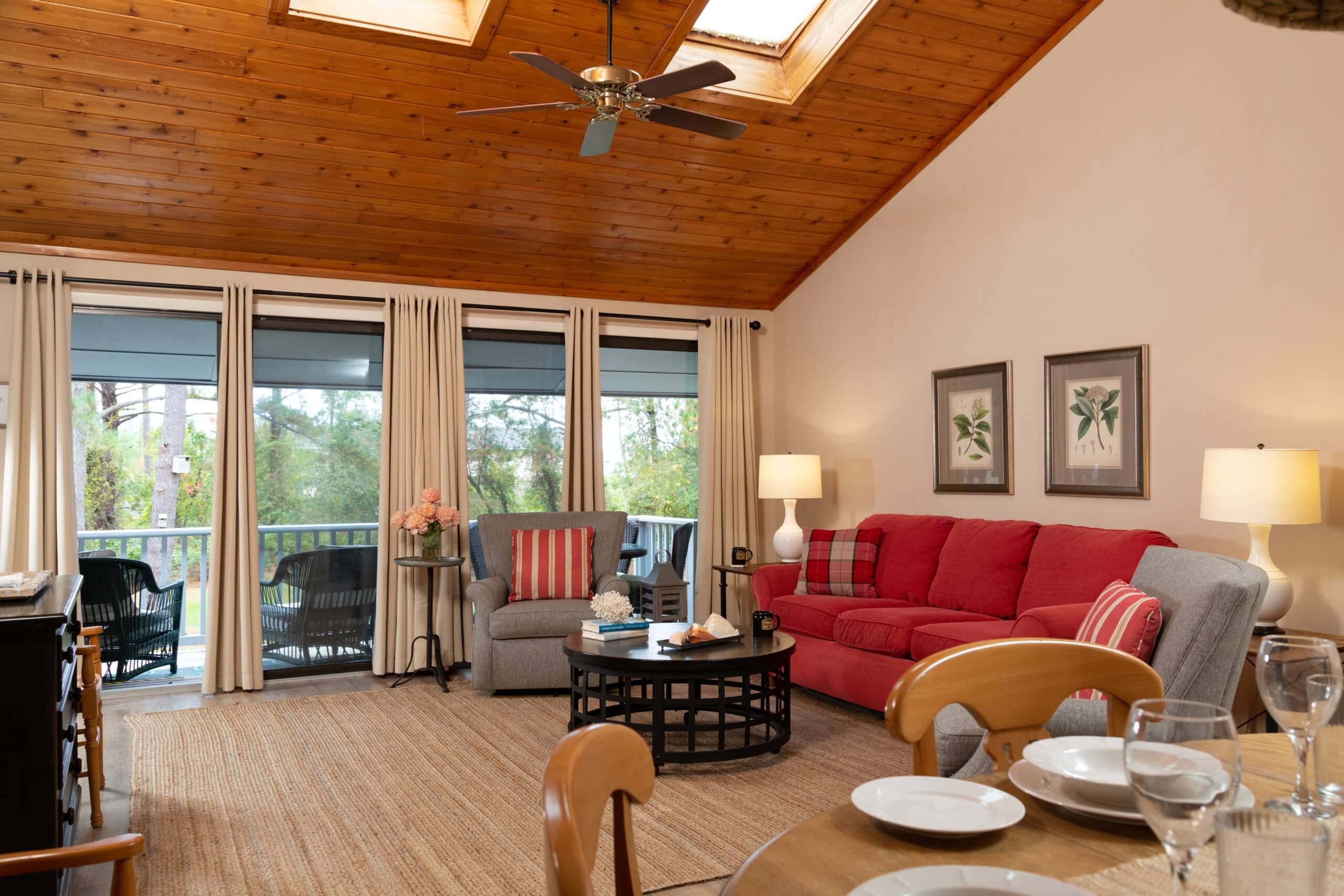 A cozy living room featuring a red sofa, gray chairs, and large windows with natural light.