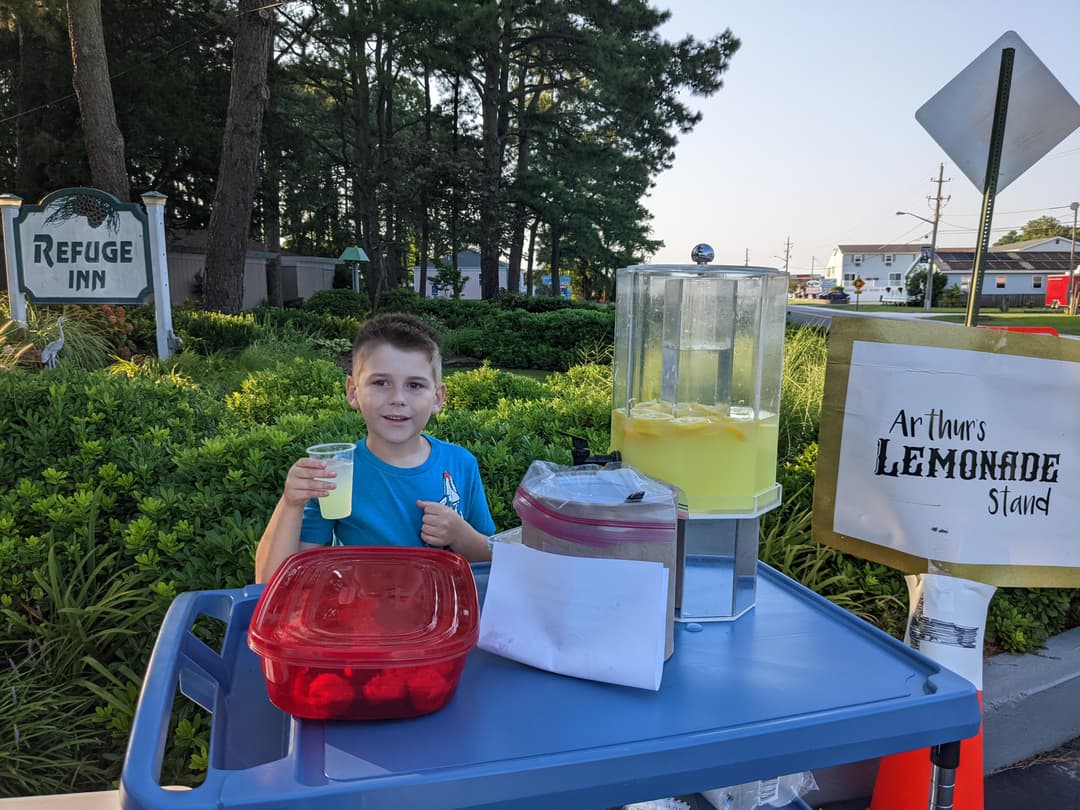 A young member of the fourth generation running a lemonade stand at the Refuge Inn sign.