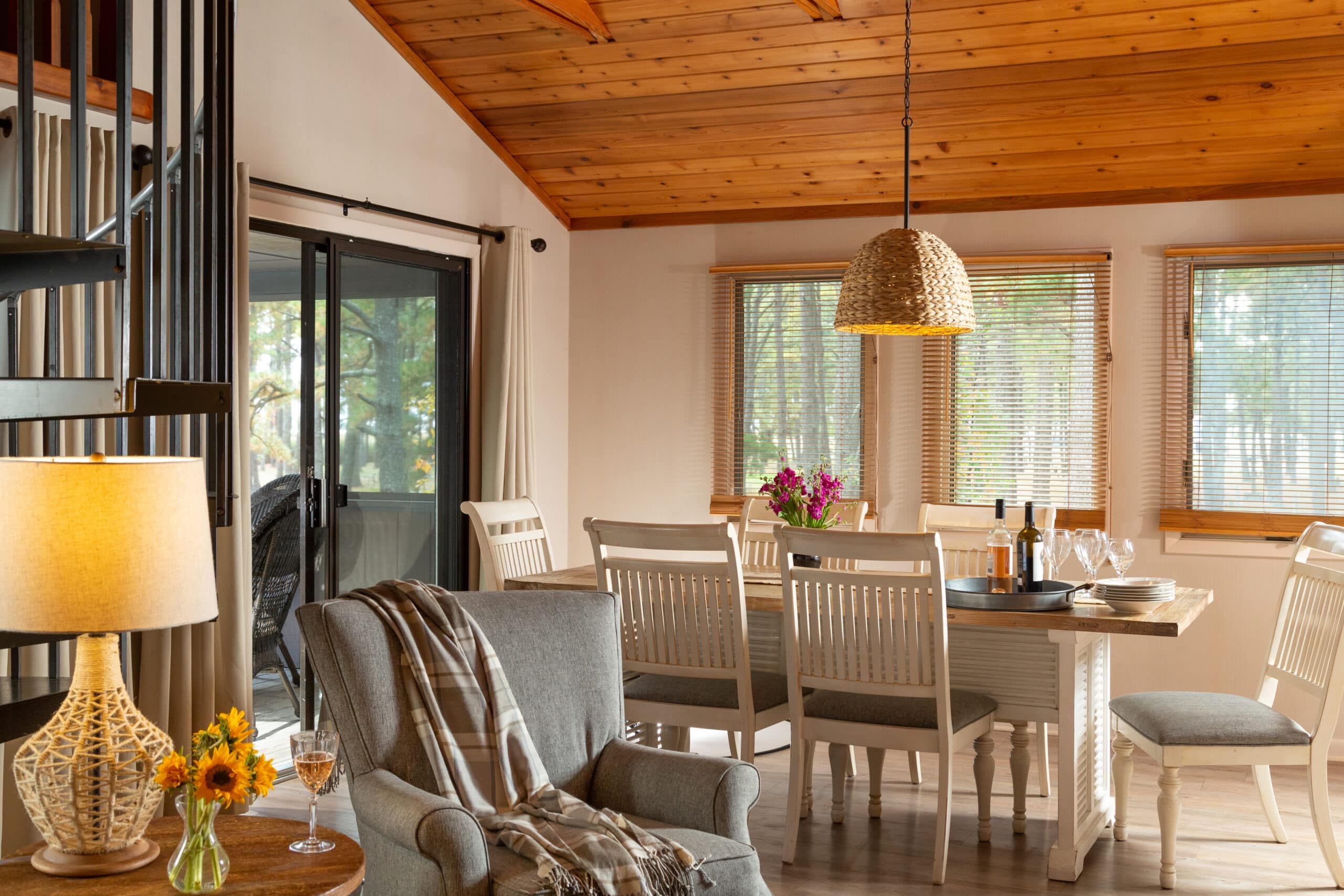 Cozy living and dining area featuring a gray armchair, wooden table, and large windows with a view of the outdoors.