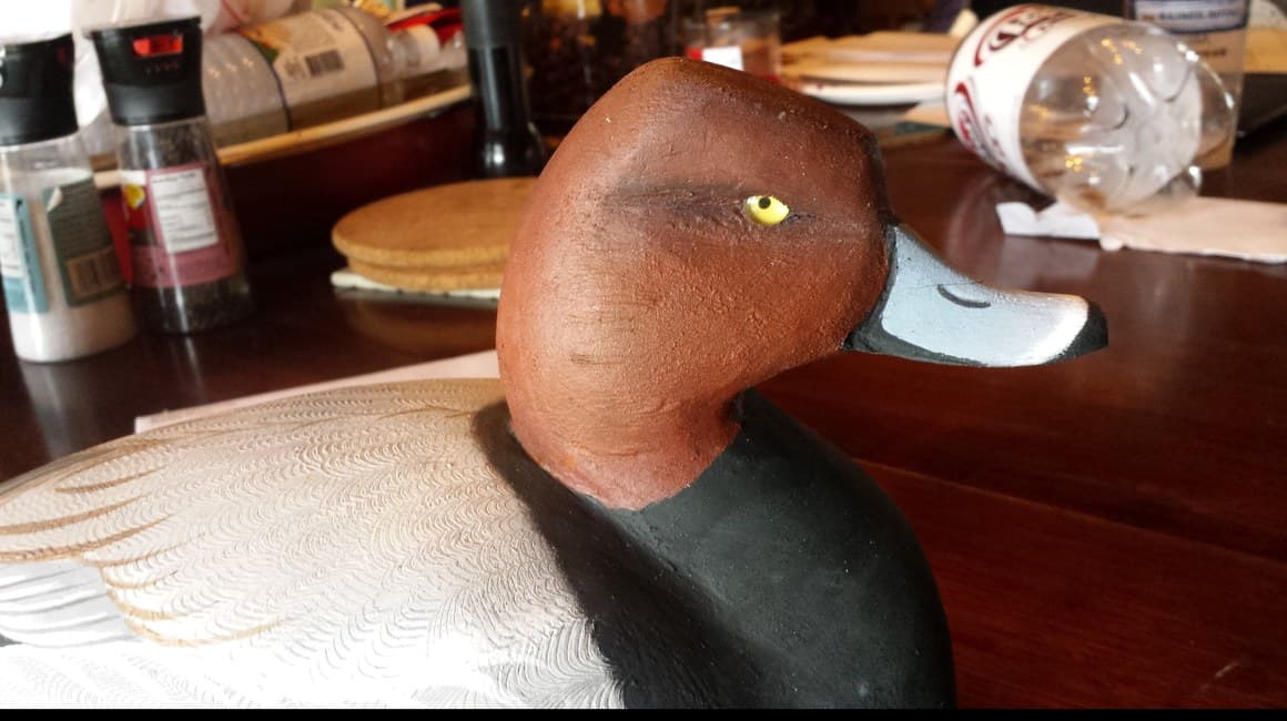A hand-carved redhead decoy on the workbench, showing the comb work on its flank and painted eye.