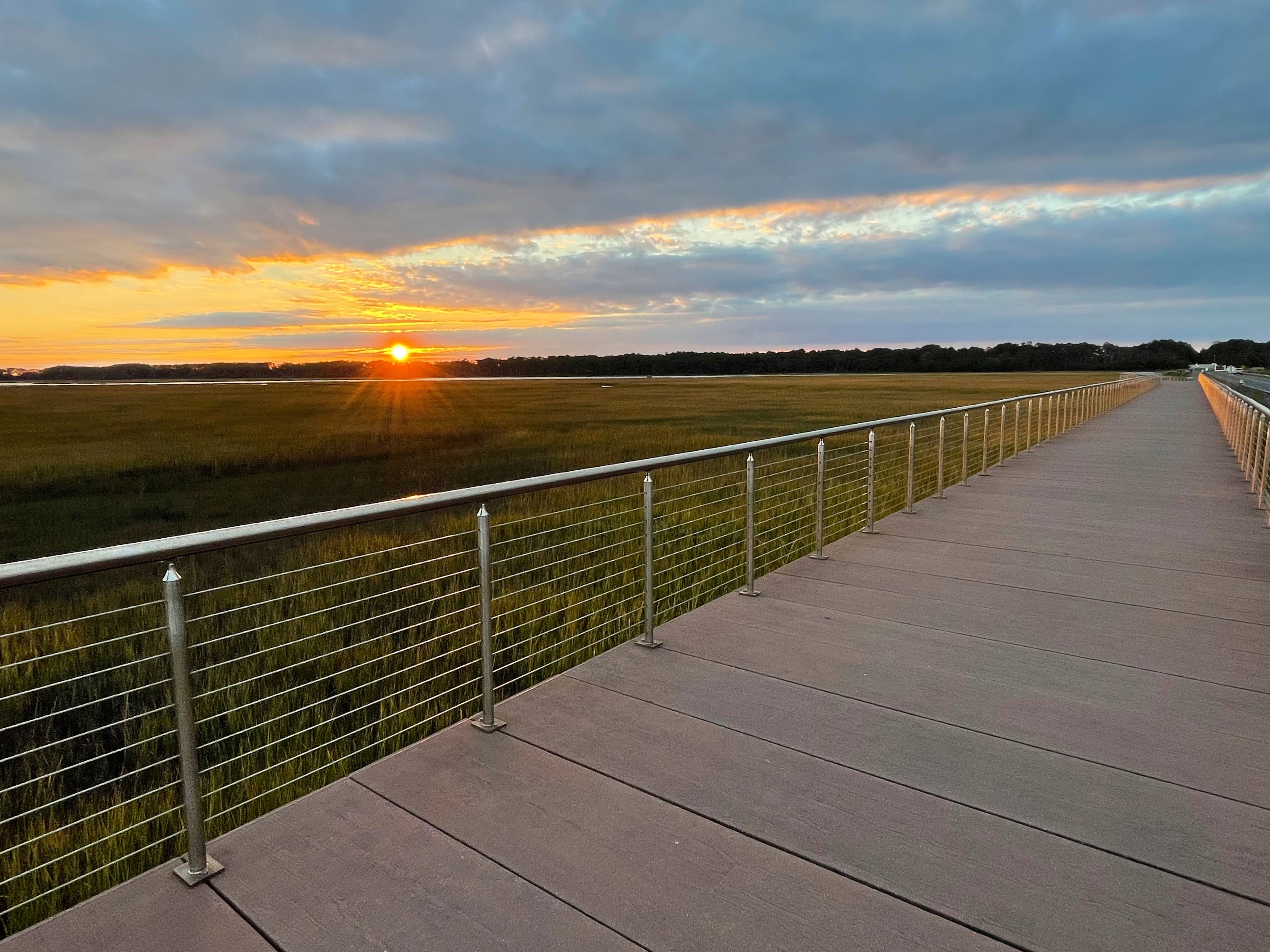 A wooden walkway leads into a sunset over a grassy marshland. A wooden walkway leads into a sunset over a grassy marshland.