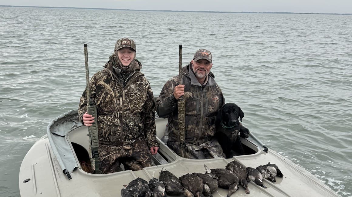 Two duck hunters and a black Labrador retriever in a boat on the water off Chincoteague Island.