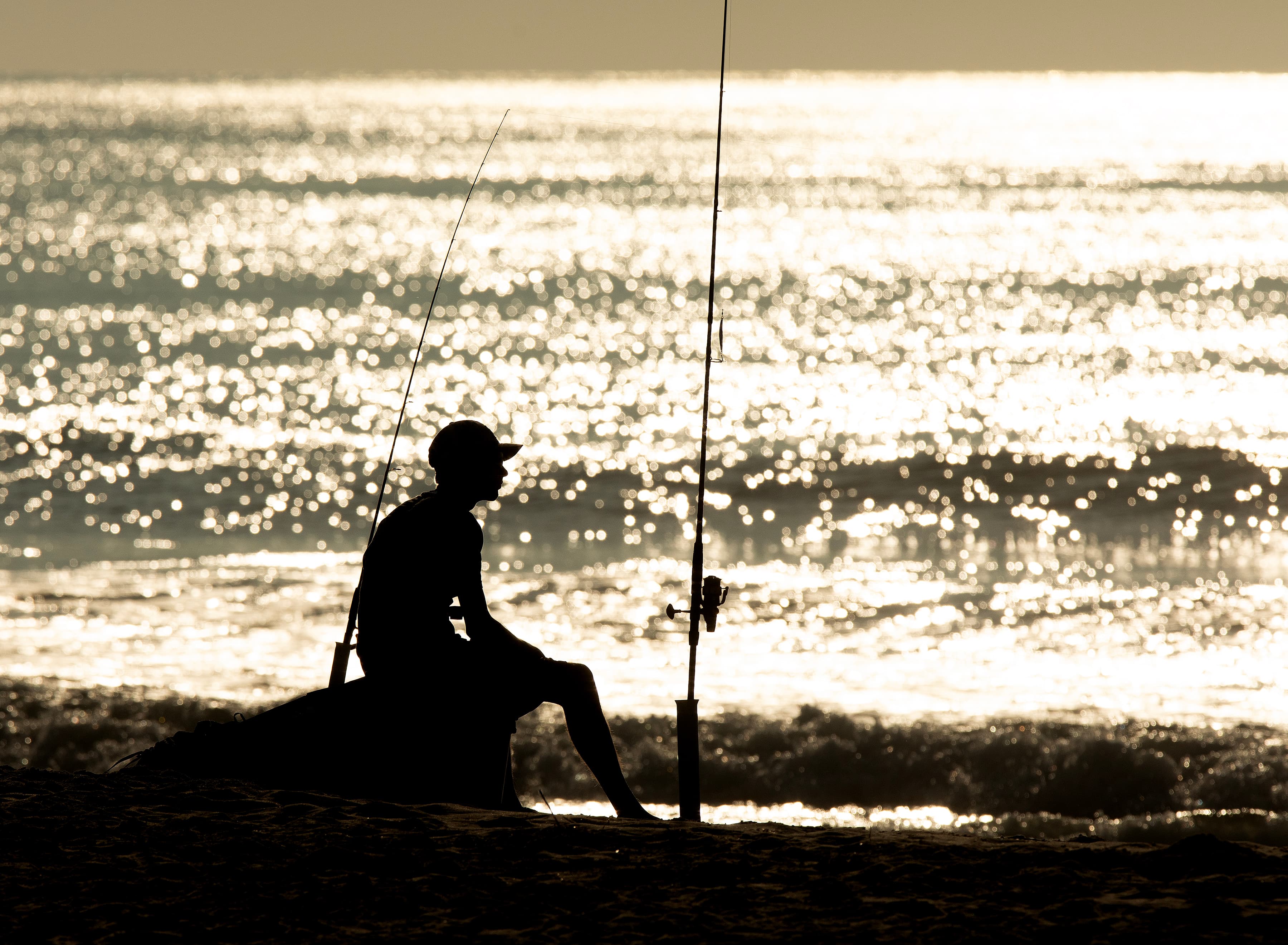 An angler in silhouette fishing the flats off Chincoteague Island at golden hour.