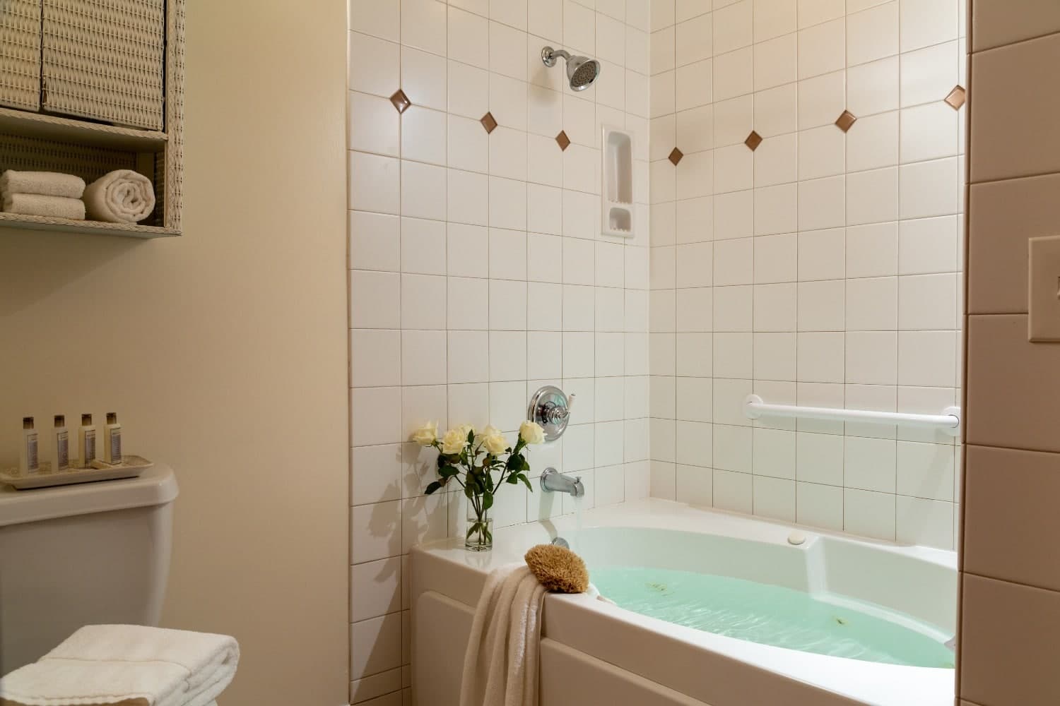 A tranquil bathroom featuring a soaking tub with green water and fresh white roses.