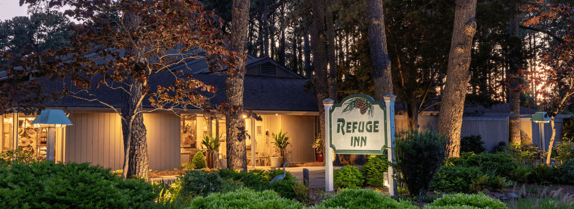 The Refuge Inn lit at dusk, its wooden sign standing among the loblolly pines on Chincoteague Island.