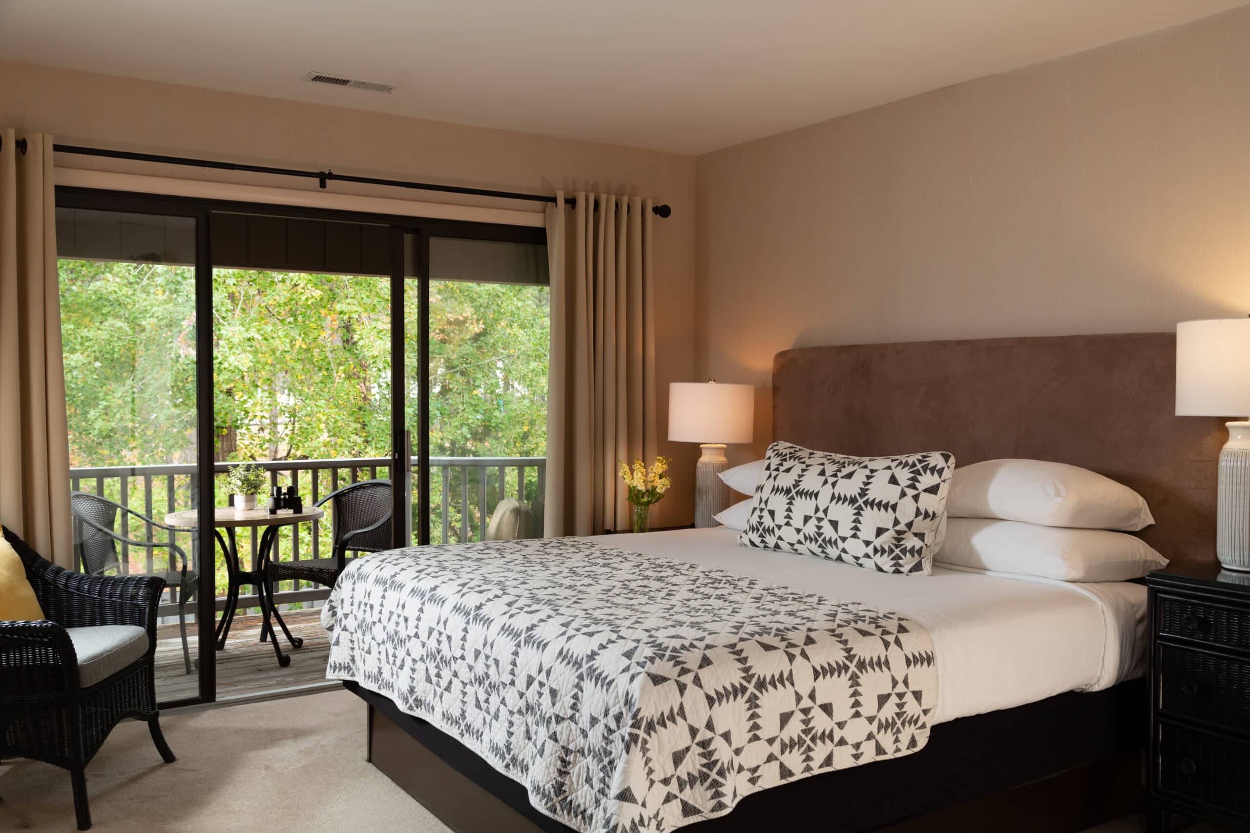 Cozy bedroom with a patterned blanket, bedside lamps, and a view of a green balcony.