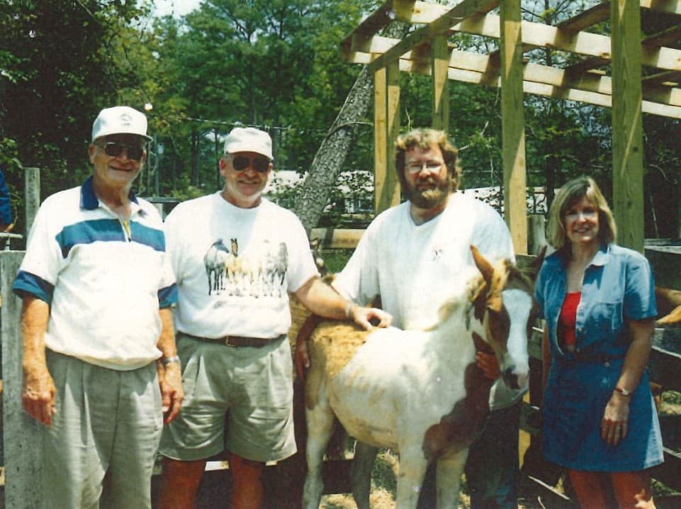 Four people standing together with a pony in a farm setting.