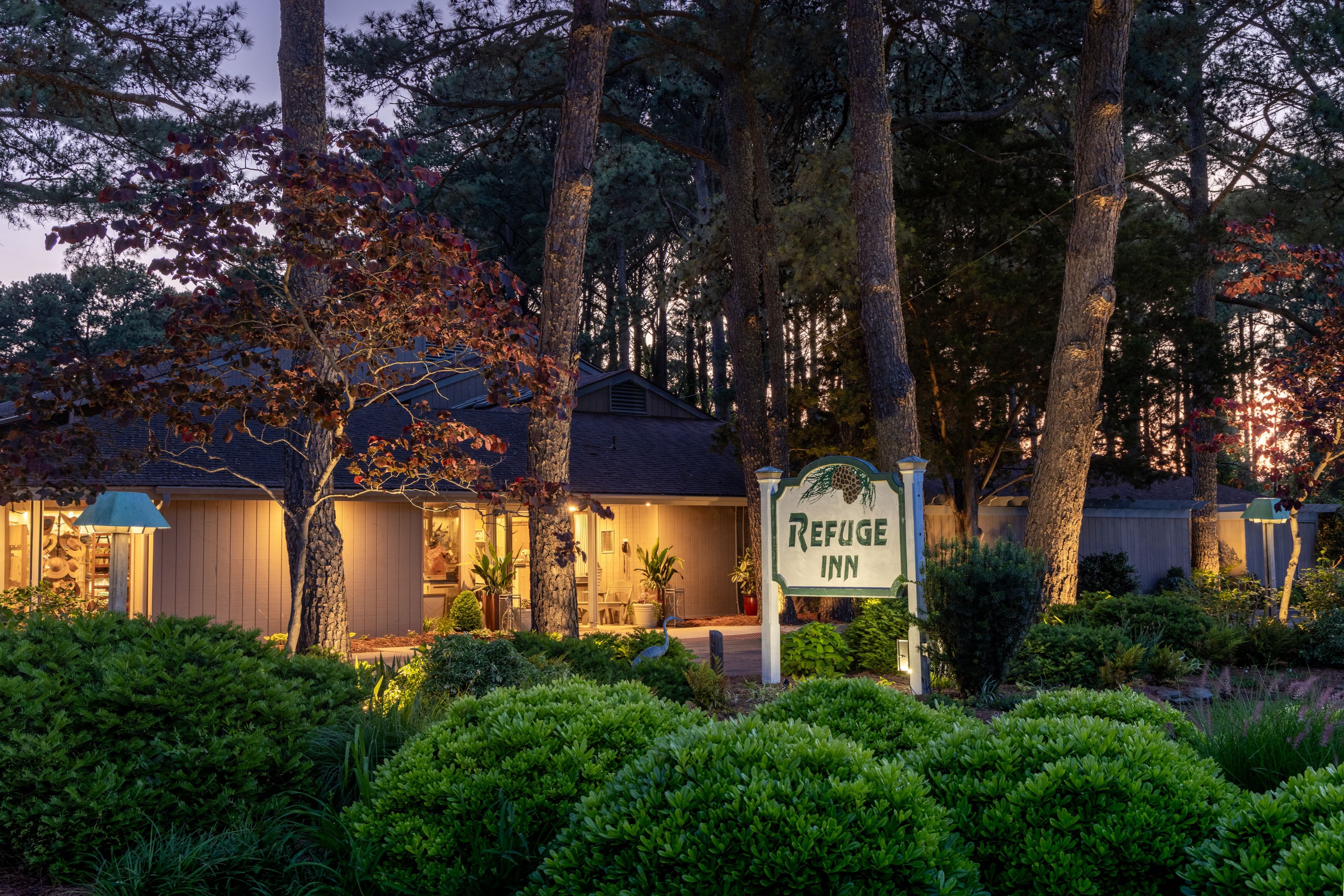 A cozy inn named Refuge Inn surrounded by lush greenery at dusk.