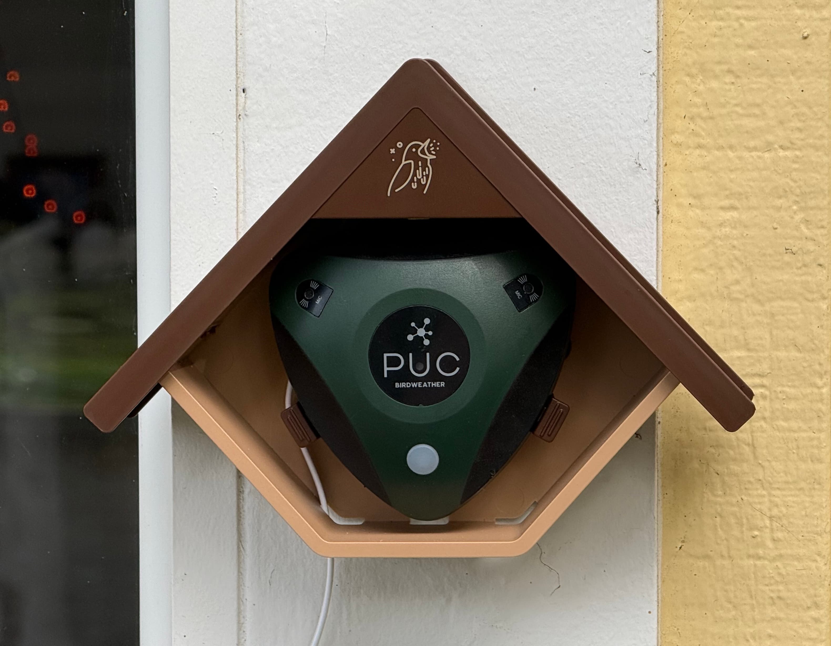 A green PUC device mounted in a house-shaped housing on a wall.