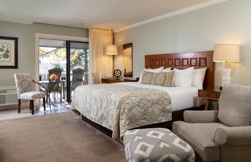 A cozy hotel room featuring a large bed, armchair, dining table, and balcony access.