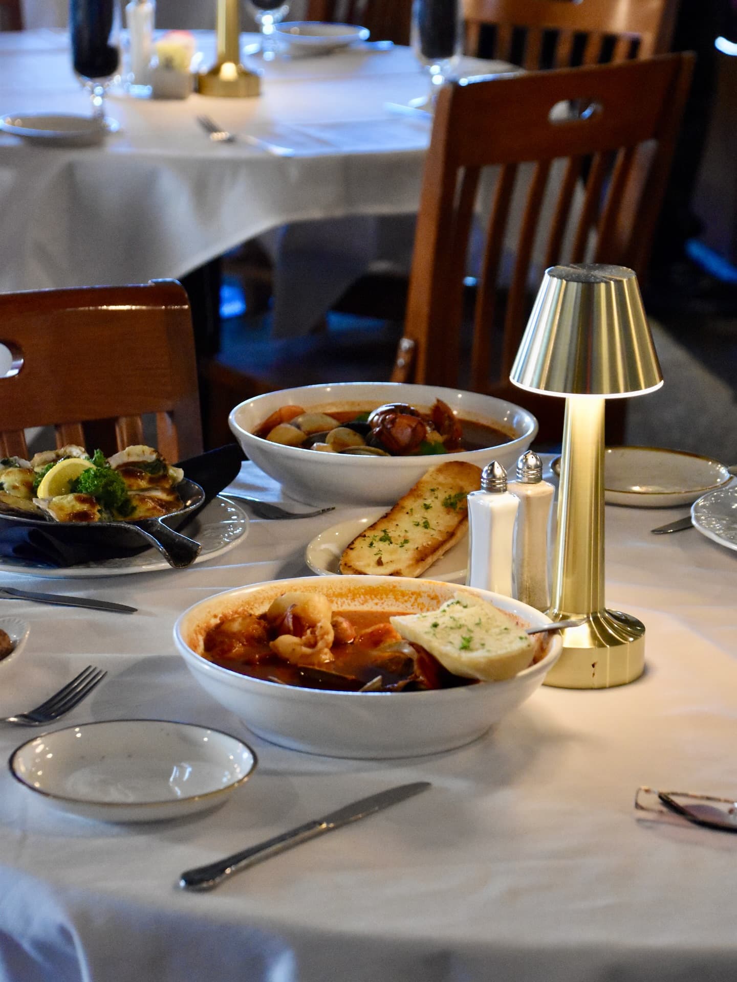 A dining table set with assorted dishes, bread, and a small lamp in a cozy restaurant setting. A dining table set with assorted dishes, bread, and a small lamp in a cozy restaurant setting.