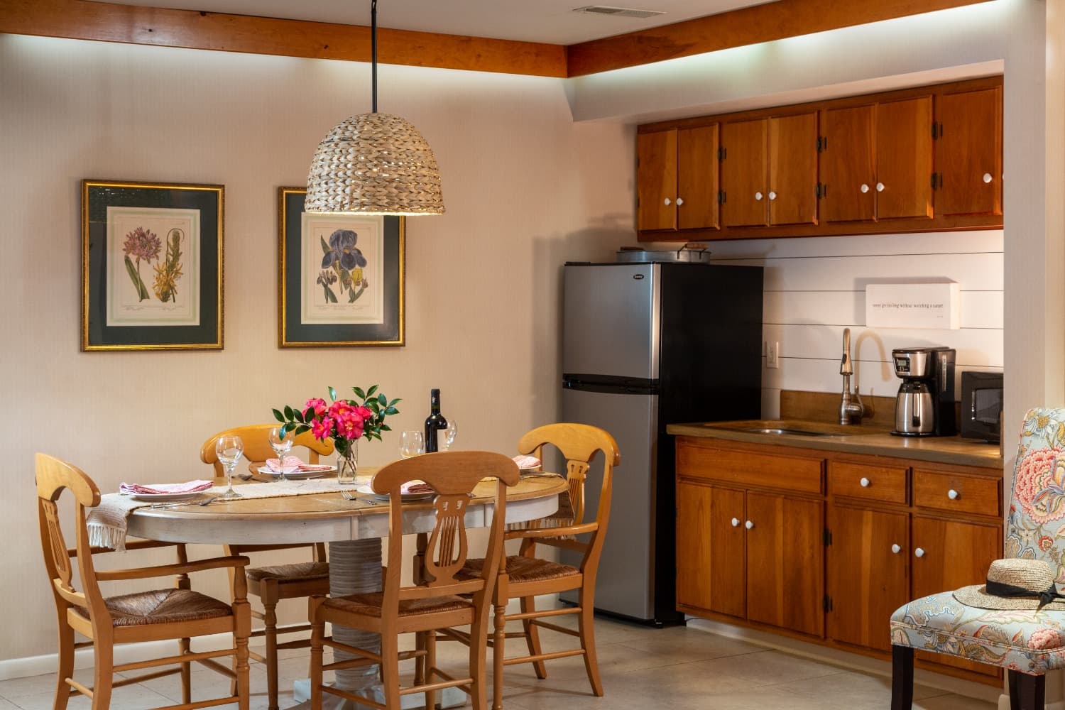 A cozy dining area with a round table, wooden chairs, and a kitchen featuring a refrigerator and cabinets.
