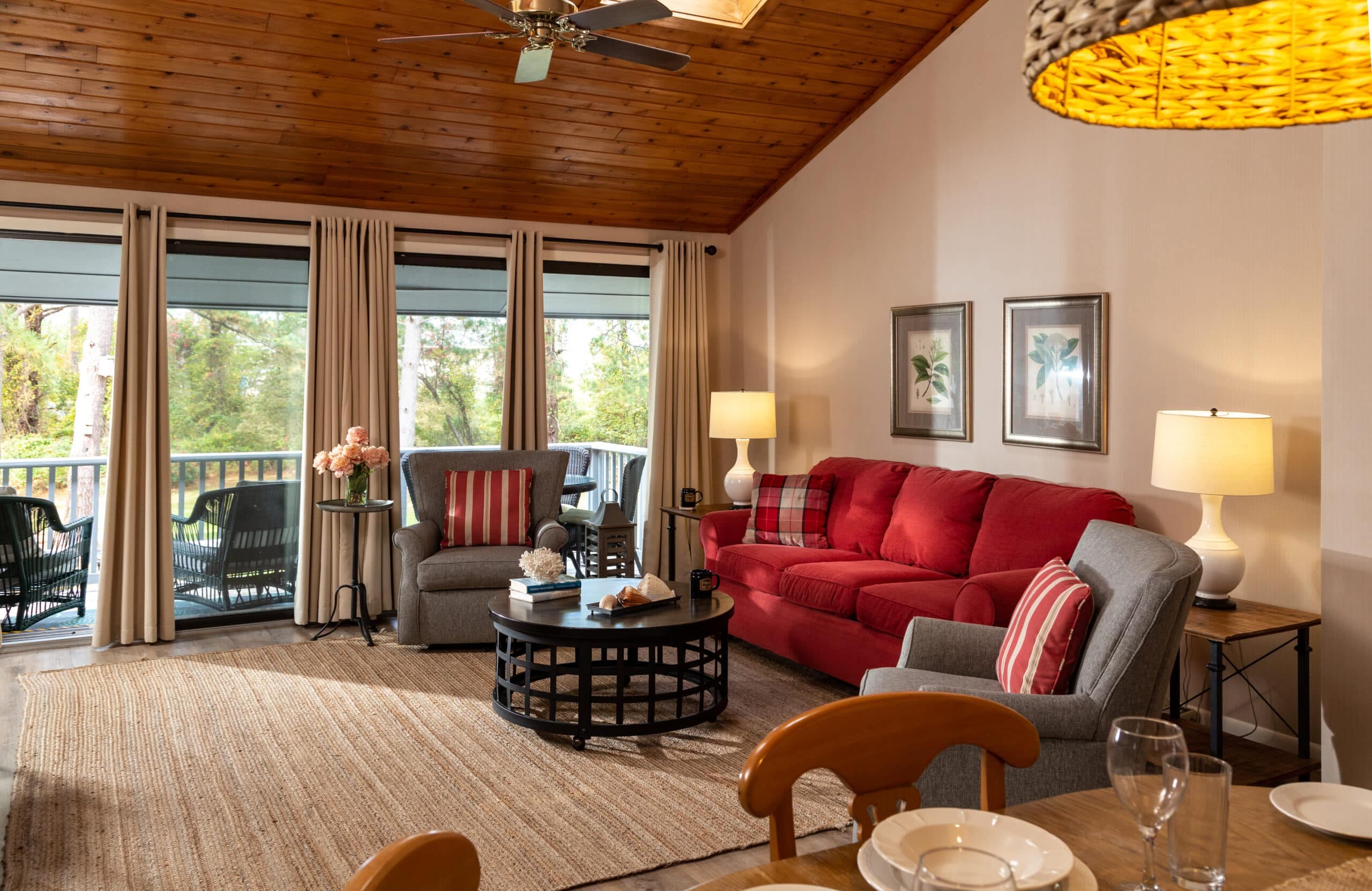 A cozy living room featuring a red sofa, grey chairs, natural wood accents, and large windows with views of greenery.