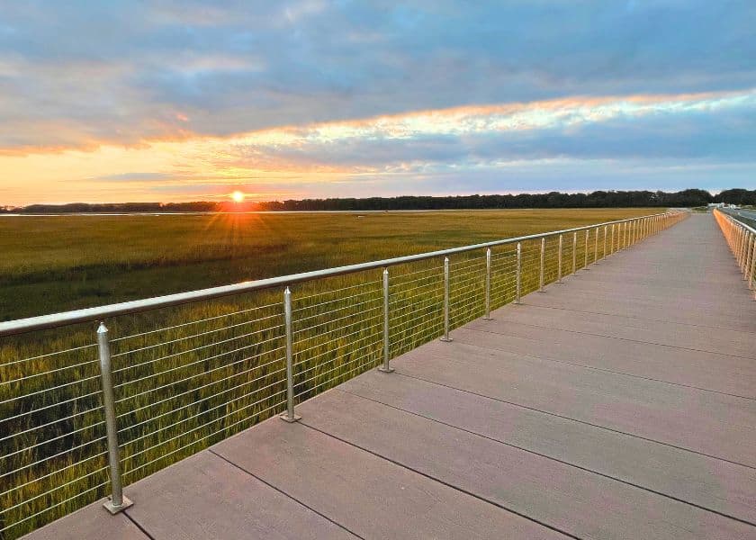 A wooden boardwalk on Chincoteague with metal cable railings stretches across marshland toward a low sunset